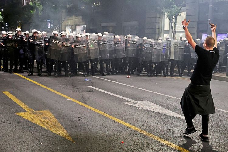 Ein Demonstrant steht einer Gruppe von Bereitschaftspolizisten mit Schilden und Helmen gegenüber und hebt gestikulierend die Arme. Die Szene spielt sich nachts auf einer Straße in Belgrad, Serbien, während eines studentengeführten Protests am 23. Mai 2026 ab.