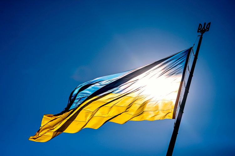 Die ukrainische Flagge weht an einem Fahnenmast vor einem sonnigen, wolkenlosen Himmel. Die Sonne scheint durch den Stoff.