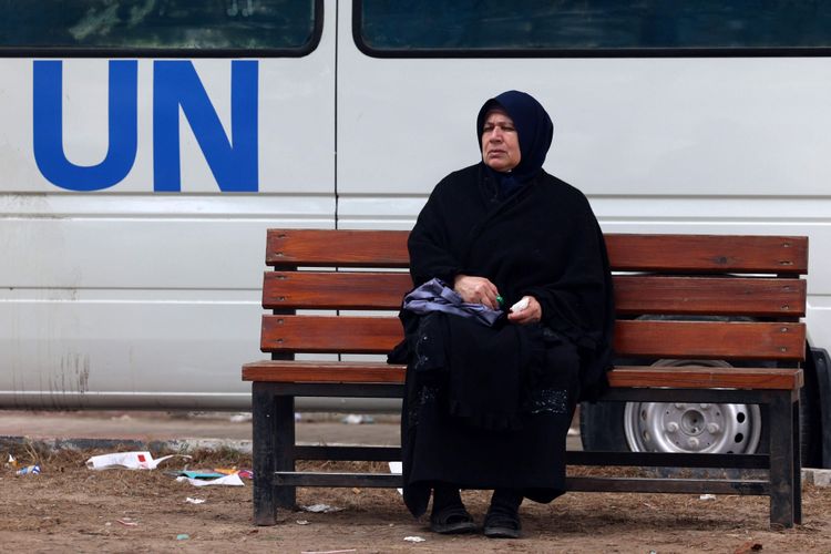 Eine Frau sitzt im Gazastreifen auf einer Bank, dahinter ein UN-Fahrzeug.