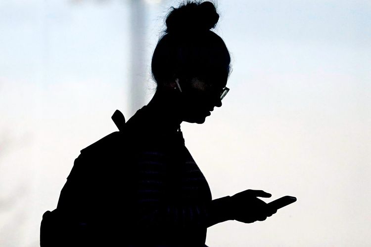 Die Silhouette einer Frau, die auf das Smartphone in ihrer Hand schaut.