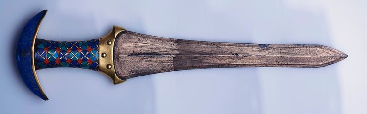 Ein verziertes antikes Messer mit einer Klinge aus Metall, einem Griff mit buntem geometrischen Muster und einer halbmondförmigen Parierstange.