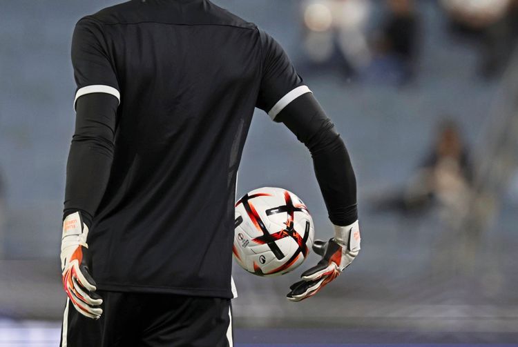 Ein Torwart in schwarzer Sportbekleidung hält einen Fußball mit einer Hand an seiner Hüfte. Aufnahme im Stadion Graz-Liebenau.