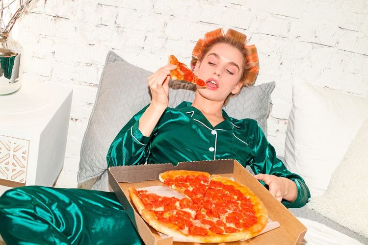 Ein Frau sitzt auf einem Sofa und isst eine Salamipizza.