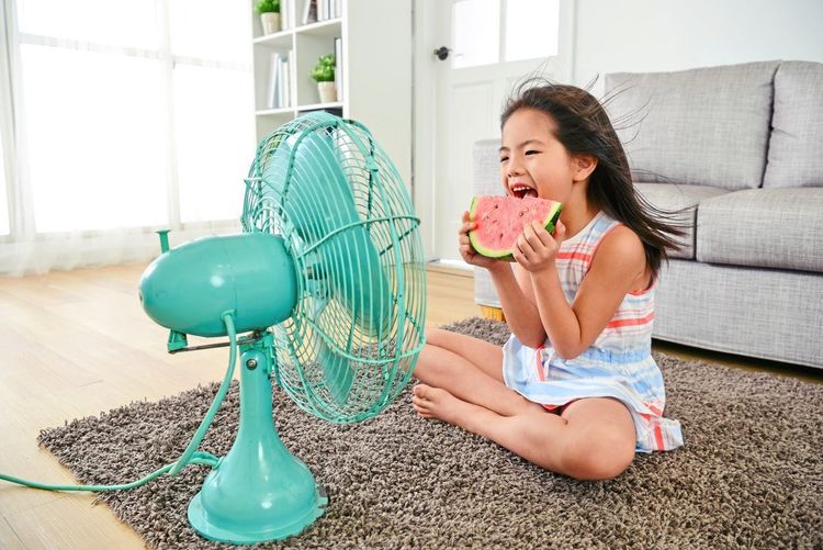 Kind isst bei Sommerhitze vor dem Ventilator eine Wassermelone.