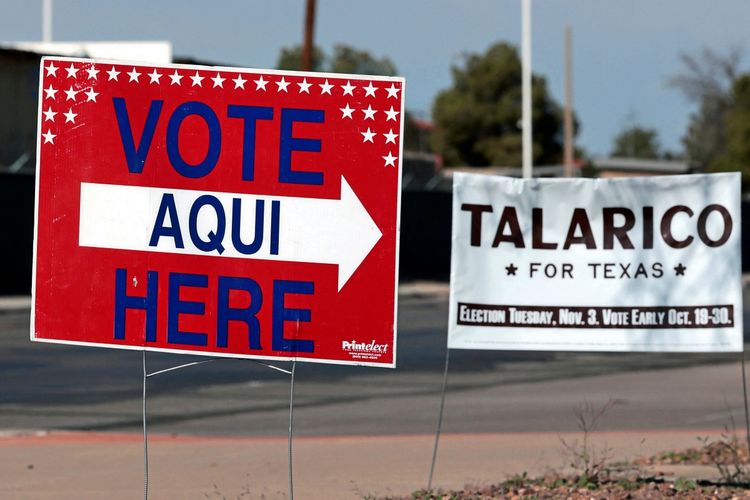 Ein rotes Schild mit der Aufschrift „Vote Aquí Here“ weist auf ein Wahllokal in El Paso, Texas, hin. Im Hintergrund ist ein weiteres Banner mit der Aufschrift „Talarico for Texas“ zu sehen.