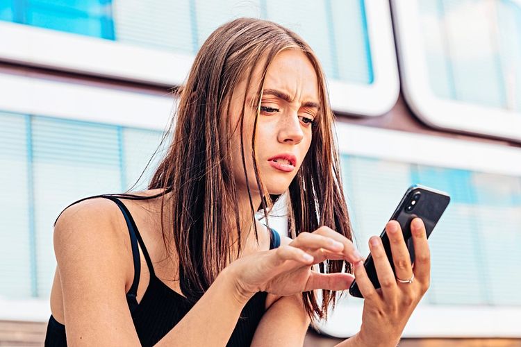 Eine Frau schaut stirnrunzelnd in ihr Handy, während sie etwas zu murmeln scheint