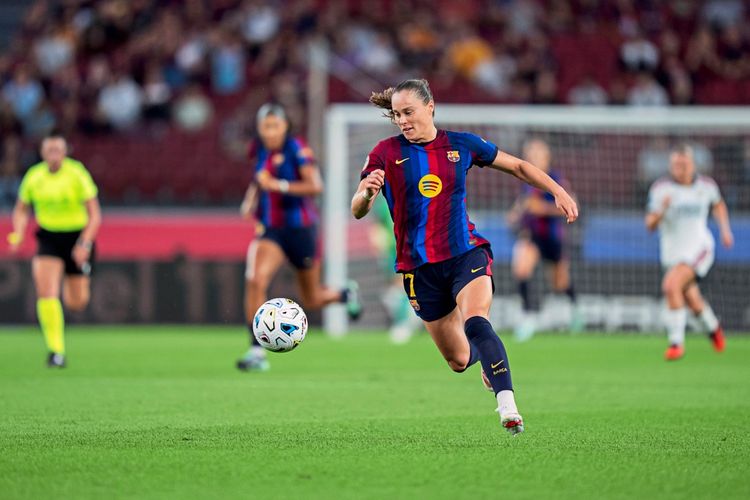 Eine Fußballspielerin im Trikot des FC Barcelona (blau-rot gestreift) sprintet auf dem Spielfeld mit Blick auf den Ball. Im Hintergrund sind Mitspielerinnen, Gegenspielerinnen, eine Schiedsrichterin in Gelb und das Tor sichtbar. Das Spiel findet im Spotify Camp Nou statt.