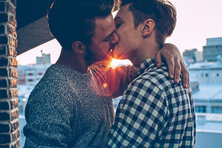 Zwei Männer küssen sich auf einer Dachterrasse, der eine hat den Arm um den Hals des anderen gelegt