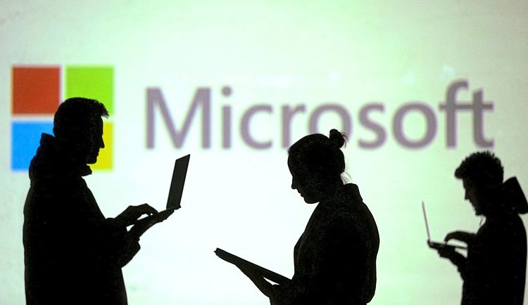 Silhouetten von Laptop-Nutzern neben einer Bildschirmprojektion eines Microsoft-Logos.