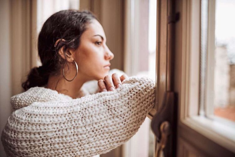 Junge Frau schaut traurig aus dem Fenster