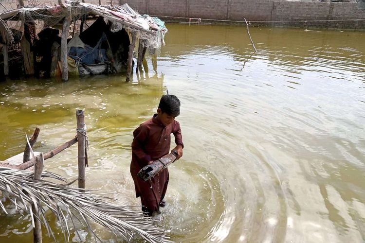 Pakistan nach Überflutung im März 2024. Junge in Wasser hält Gegenstand.