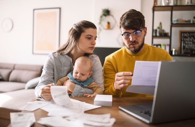 Familie mit Baby vor Computer schaut besorgt auf ein Stück Papier
