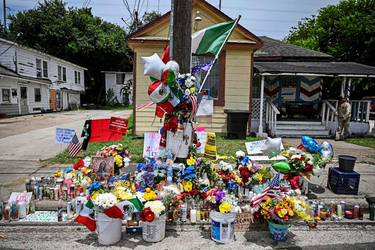 Gedenkstätte mit Blumen, Kerzen, Luftballons und handgeschriebenen Botschaften in einer Wohngegend vor einem gelben Haus. Mexikanische und US-amerikanische Flaggen sind sichtbar, umgeben von zahlreichen Opferbekundungen.