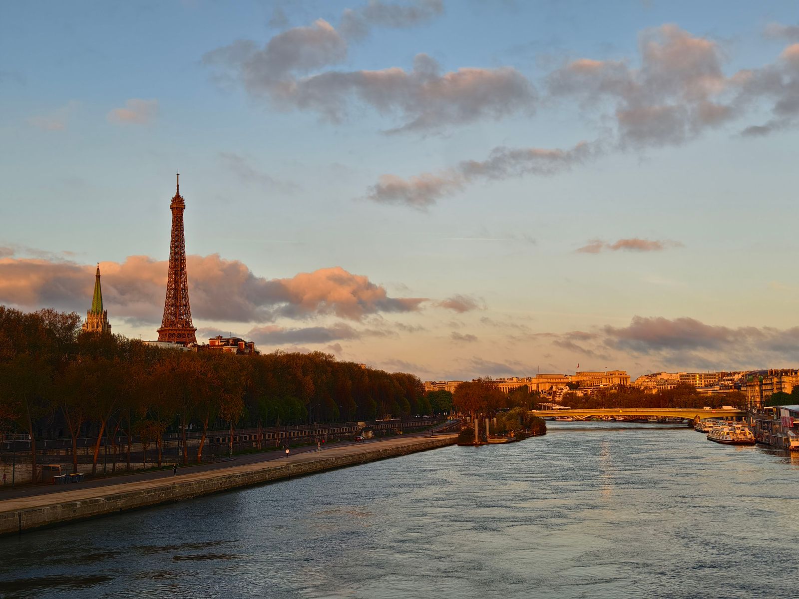 Ein Fluss in einer Stadt bei Sonnenaufgang, am linken Ufer im Hintergrund ist der Eiffelturm zu sehen