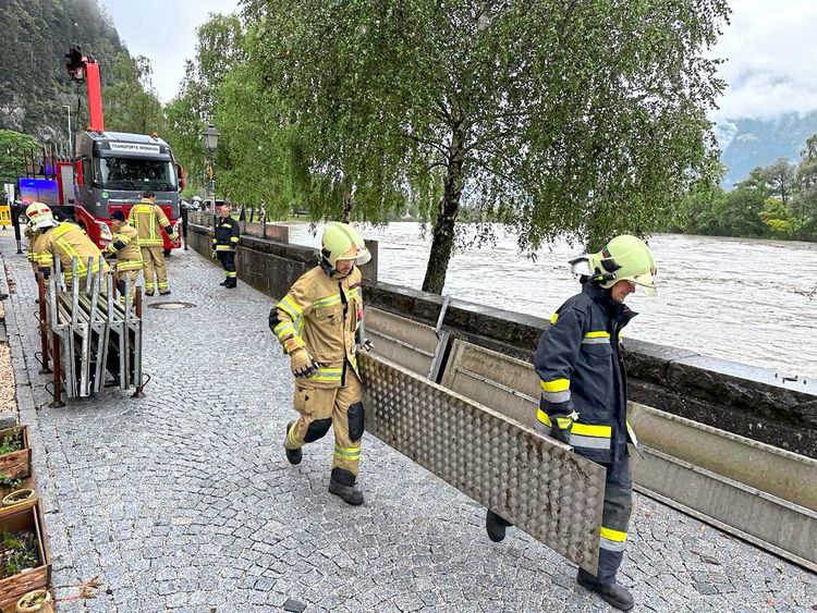 Mehrere Feuerwehrleute sind vor einem Hochwasser führenden Fluss zu sehen.