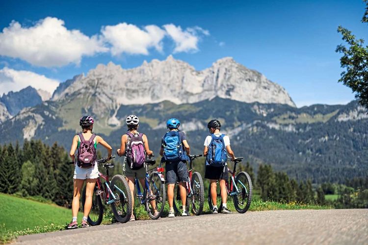 Vier Personen stehen mit Fahrrädern am Rand eines Weges, im Hintergrund ist Gebirge zu sehen.
