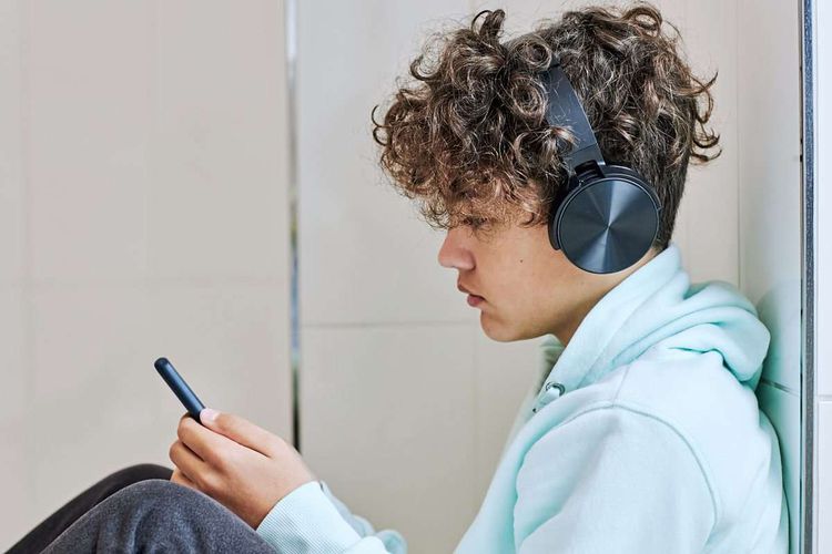 Jugendlicher mit Kopfhören schaut auf sein Smartphone