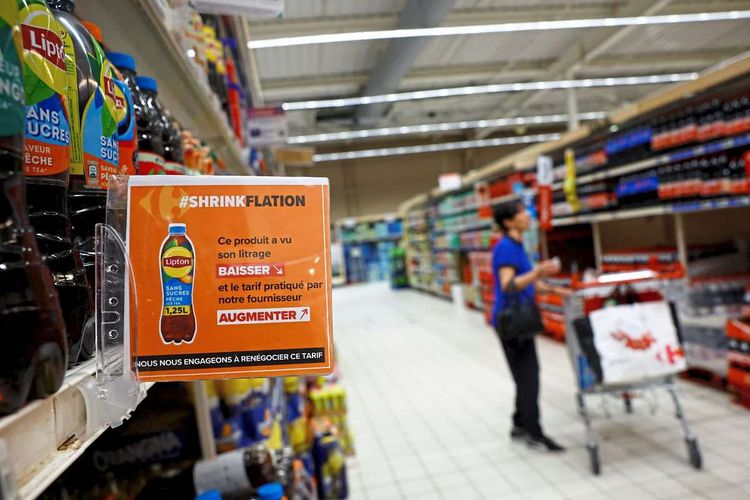 Ein Supermarktregal mit einem großen, orangen Hinweisschild, das auf die verringerte Füllmenge eines Softdrinks hinweist.