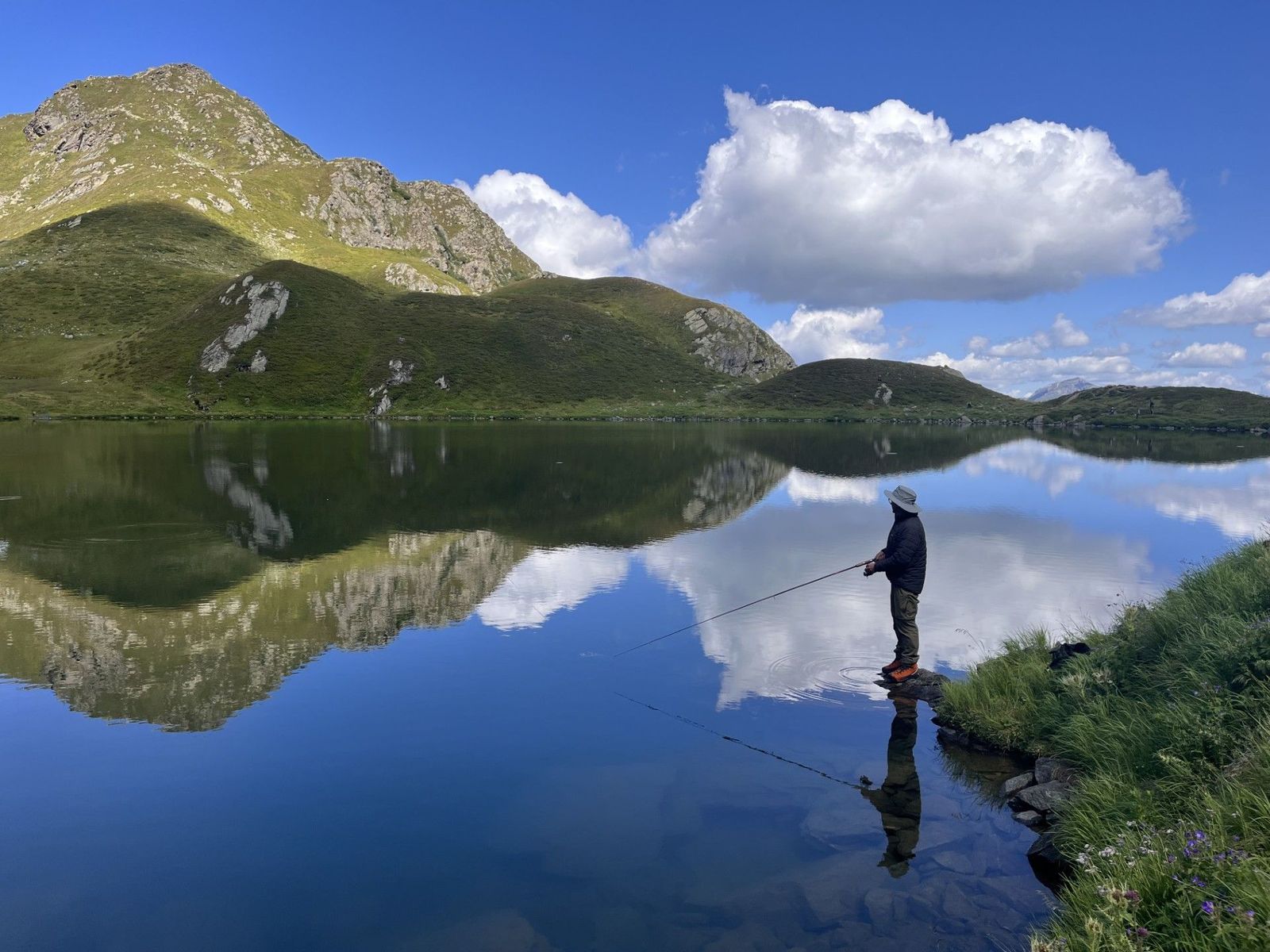 Ein Mann fischt in einem klaren Bergsee.