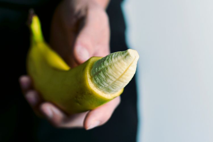 Nahaufnahme einer Hand, die eine Banane mit teilweise entfernter Schale am oberen Ende hält.
