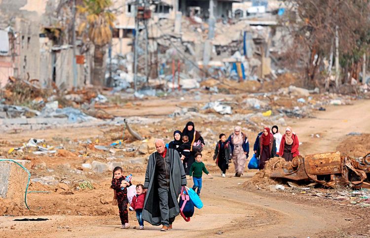 Ein Mann, mehrere Frauen und Kinder auf einem Pfad zwischen zerstörten Häusern.