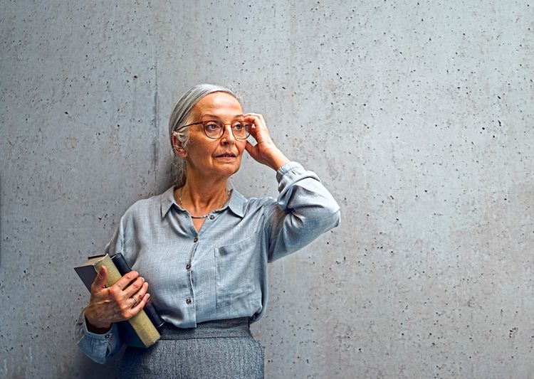 Ältere Frau mit einem Buch in der Hand vor einer Betonwand.