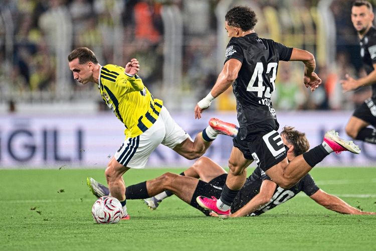 Ein Fußballspiel zwischen Fenerbahçe und Sturm Graz im Chobani-Stadion in Istanbul, Türkei. Ein Spieler von Fenerbahçe im gelb-blauen Trikot kämpft um den Ball gegen einen Spieler von Sturm Graz im schwarzen Trikot. Weitere Spieler sind im Hintergrund zu sehen.