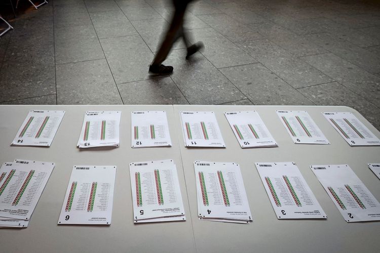 Ein Tisch mit nummerierten Stapeln von Wahlzetteln in einem Wahllokal. Im Hintergrund geht eine Person vorüber. Fotografie aufgenommen bei den Parlamentswahlen in Lettland am 3. Oktober 2026 in Riga.