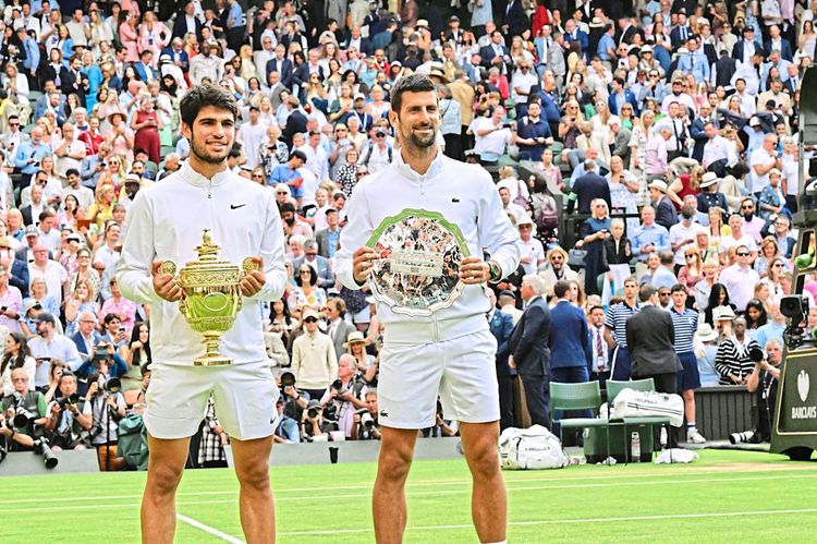 Das Bild zeigt die Siegerehrung von Wimbledon. Carlos Alcaraz und Novak Djokovic stehen nebeneinander und halten ihre jeweiligen Trophäen.