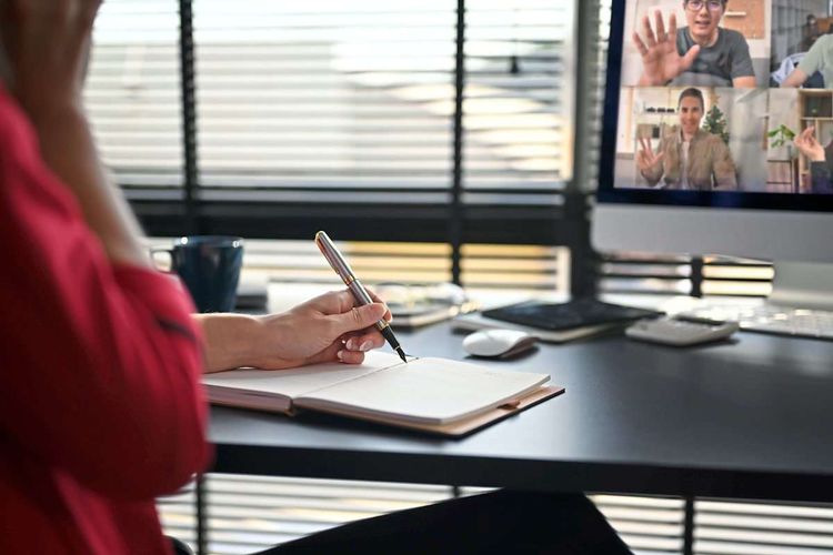 Eine Person sitzt am Computer und telefoniert via Video mit anderen.