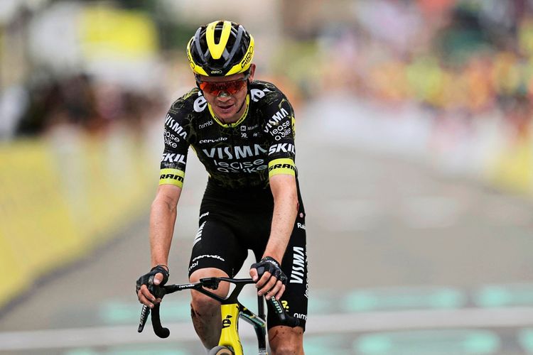 Ein Radfahrer des Teams Visma | Lease a Bike, gekleidet in einem schwarzen Trikot mit gelben Akzenten und einer gelb-schwarzen Helm, fährt erschöpft auf der Zielgeraden einer Etappe der Tour de France in einer alpinen Umgebung.