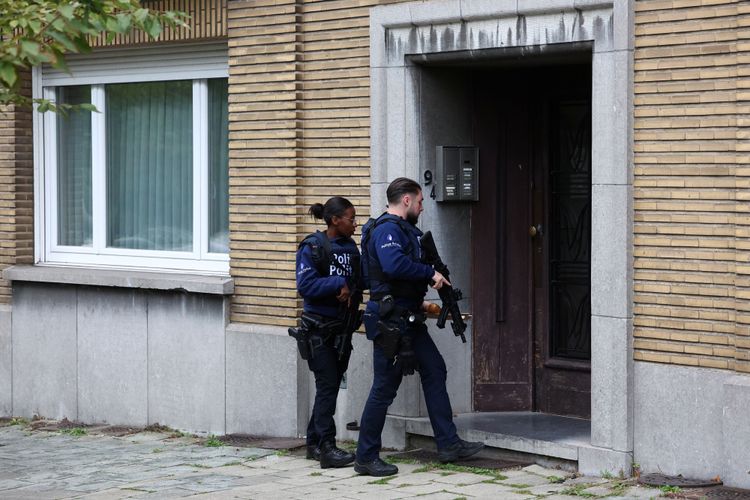 Eine Polizistin und ein Polizist mit Waffen gehen in einen Hauseingang in der Brüsseler Gemeinde Schaerbeek.