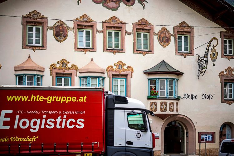 Ein bemaltes historisches Gebäude mit der Aufschrift „Weiße Rose“ und kunstvollen Verzierungen. Im Vordergrund steht ein roter LKW mit der Aufschrift „hte-gruppe.at E logistics“.