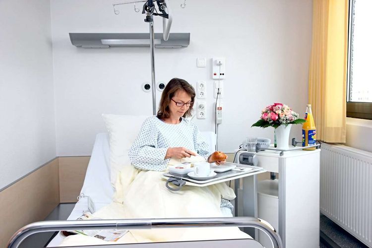 Frau in Krankenhausbett isst von einem Tablett