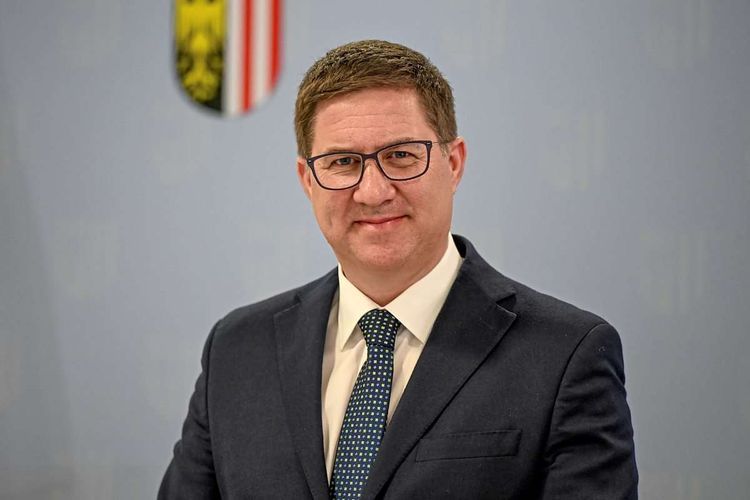 Rabl in Anzug vor Oberösterreich-Wappen.