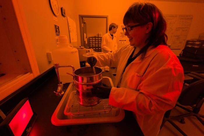 Eine Forscherin in einem Labormantel hantiert mit einem metallenen Probenbehälter.