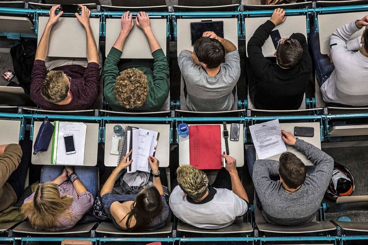 Ansicht von oben auf eine Gruppe von Studierenden in einem Hörsaal. Sie sitzen an Tischen und haben vor sich Unterlagen, Tablets, Smartphones und Schreibmaterialien. Die Szene zeigt eine Einführungsvorlesung an der Johannes Gutenberg-Universität Mainz.