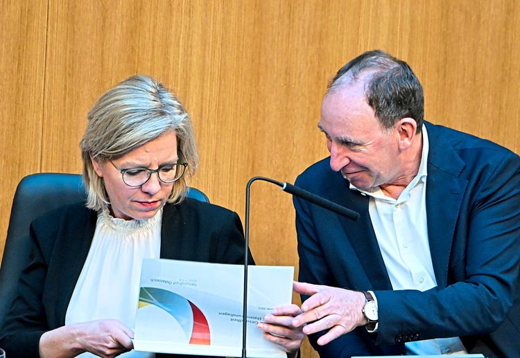 Leonore Gewessler und Johannes Rauch sitzen im Parlament und schauen gemeinsam in eine Unterlage. 