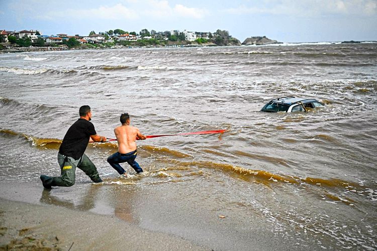 Auto versinkt im Wasser am Strand. Zwei Männer versuchen, das Auto aus dem Meer zu ziehen. 