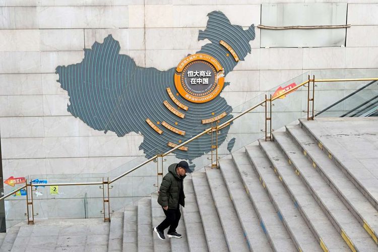Ein Mann geht Stiegen bei einem Evergrand-Komplex hinauf. Im Hintergrund ist eine Karte Chinas zu sehen.
