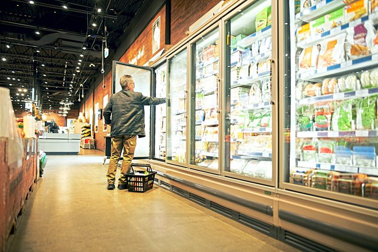 Ein Mann greift in einem Supermarkt in ein Tiefkühlregal.