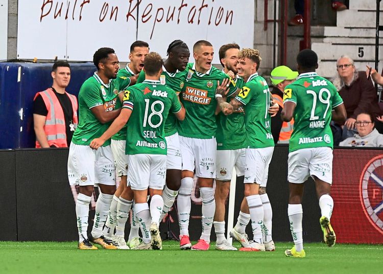 Eine Gruppe von Spielern des SK Rapid Wien in grünen Trikots feiert gemeinsam auf dem Spielfeld ein Tor während eines Spiels der UEFA Europa Conference League Play-Offs gegen Heart of Midlothian im Tynecastle Park, Edinburgh. Im Hintergrund sitzen Zuschauer auf der Tribüne.