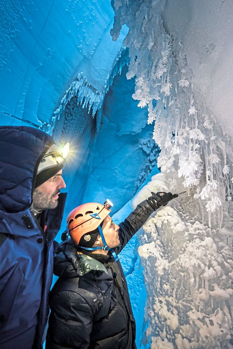 Zwei Höhlenforscher vor einer Eiswand mit Eiszapfen, an denen sich besondere Kristallstrukturen gebildet haben