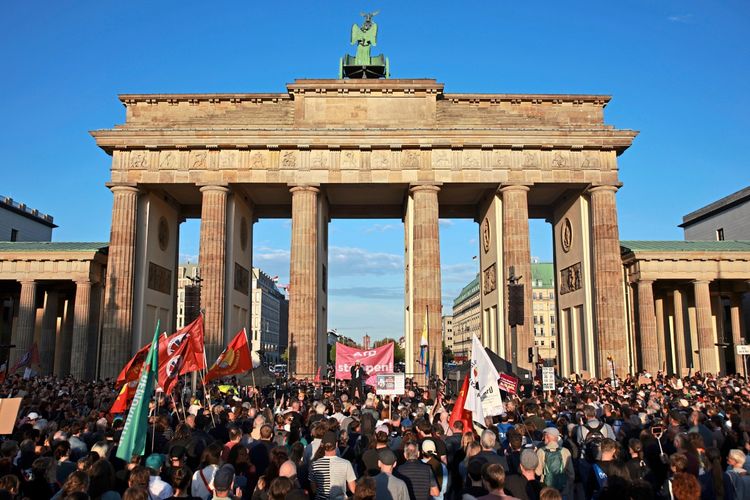 Menschenmassen versammeln sich vor dem Brandenburger Tor in Berlin bei einer Kundgebung. Teilnehmer halten Plakate und Fahnen, während die Abendsonne das Wahrzeichen beleuchtet.