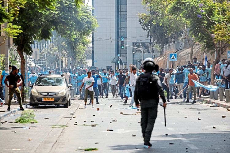 Demonstrierende im Hintergrund, Polizist im Vordergrund in Tel Aviv