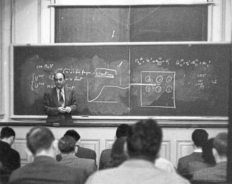 Enrico Fermi vor einer Tafel, davor ein paar Reihen von Schülern