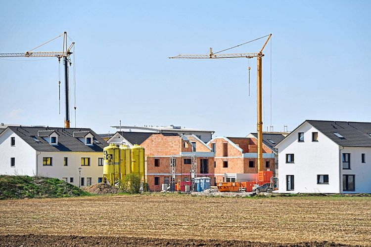 Kräne und Bauschutt zwischen Neubauwohnungen in einer ländlichen Siedlung.