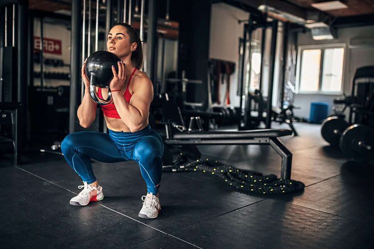 Junge Frau macht im Fitnessstudio Kniebeugen mit Kettlebell vor der Brust