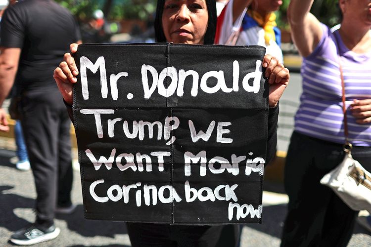 Eine Frau hält bei einer Protestkundgebung in Caracas, Venezuela, am 28. Juli 2026 ein schwarzes Schild mit der handgeschriebenen Botschaft: „Mr. Donald Trump, we want Maria Corina back now“. Im Hintergrund sind weitere Demonstrierende zu sehen.