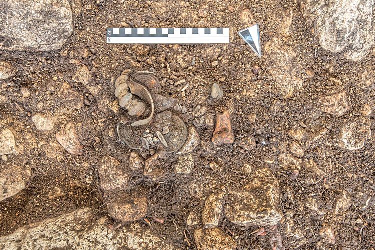 Ein Detail des gefundenen Grabes mit einigen aus der Erde ragenden Schmuckgegenständen und Knochen.